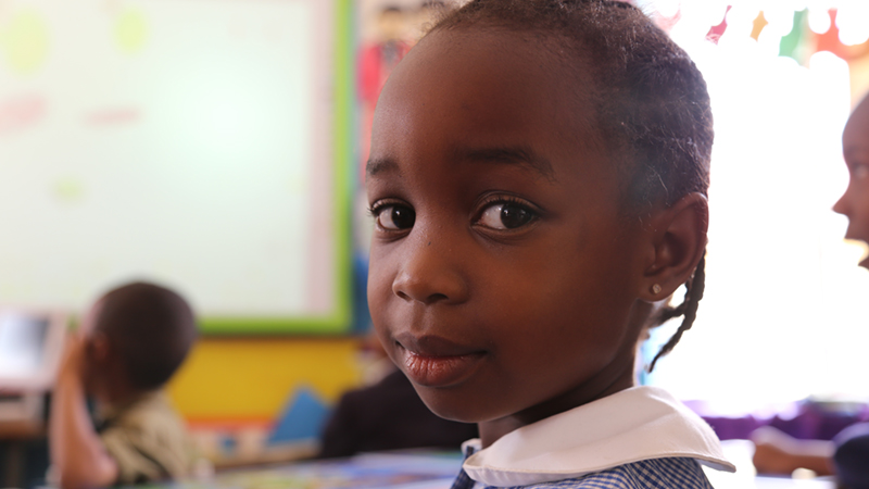 Credit/ALT text: A school girl smiles at the camera. Avondale Infant School, Zimbabwe. Credit: GPE/ Carine Durand